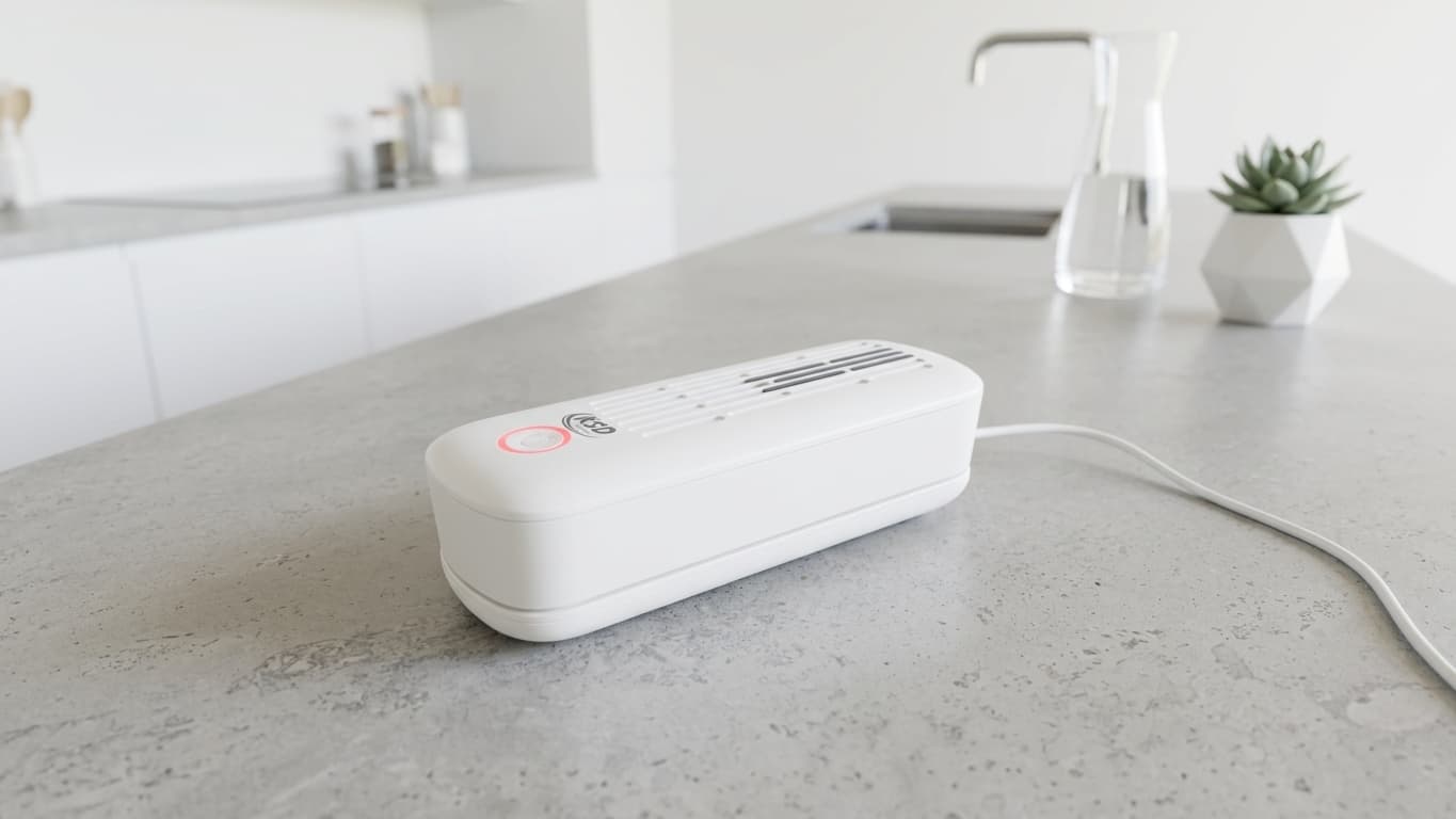 KSD Cleaner charging wirelessly on a grey concrete kitchen counter, red indicator light on during recharge, in a clean modern white kitchen
